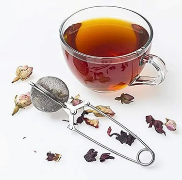 Clear glass mug with tea and tea leaves, metal tea infuser on a white background